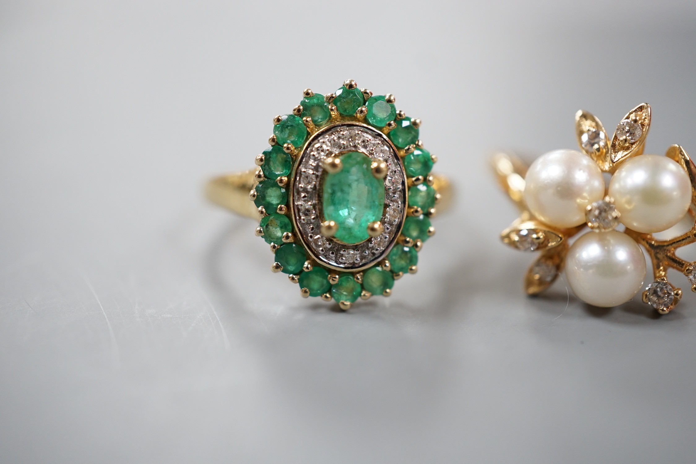 A modern yellow metal, cultured pearl and diamond chip set flower head cluster ring, size K and a 9ct, emerald and diamond chip set cluster ring, gross weight 6.8 grams.